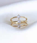 The Indy Ring by Kinsey Designs Archives is a gold filled ring with three bands, each set with a round cubic zirconia, shown on a white fabric background.