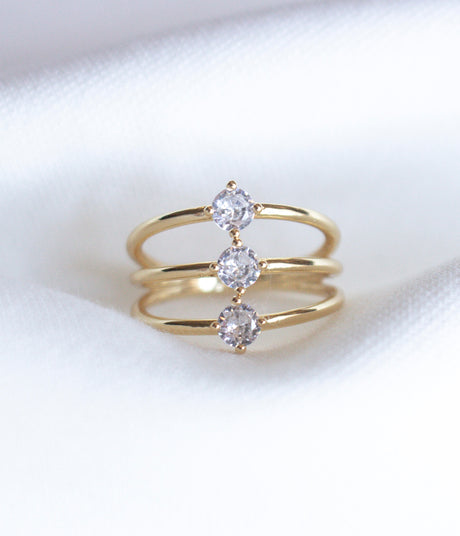 The Indy Ring by Kinsey Designs Archives is a gold filled ring with three bands, each set with a round cubic zirconia, shown on a white fabric background.