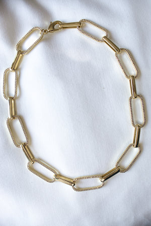 The Jameson Necklace by Kinsey Designs features large rectangular gold links, beautifully displayed on white fabric, making it a perfect bold statement piece.