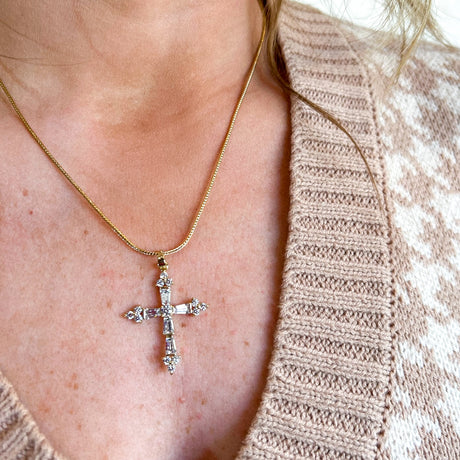 The Jamie Necklace by Kinsey Designs Archives features a gold filled 18" chain with a jeweled cubic zirconia cross pendant, elegantly layered over a beige patterned sweater.