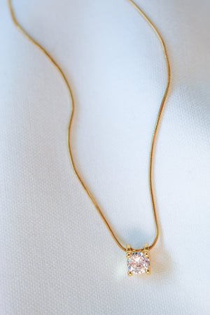 The Jenna Necklace by Kinsey Designs Archives features a single round diamond pendant on an elegant 18-inch gold filled chain, displayed on a white fabric background.