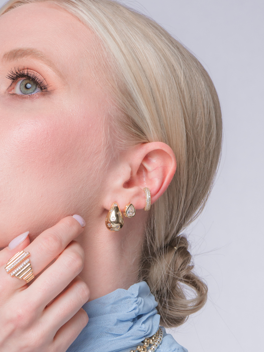 A woman with blonde hair in a low bun wears the Kinsey Designs Archives Kline Dome Earring (0.75" long, gold filled), a gold ring, and a blue top.
