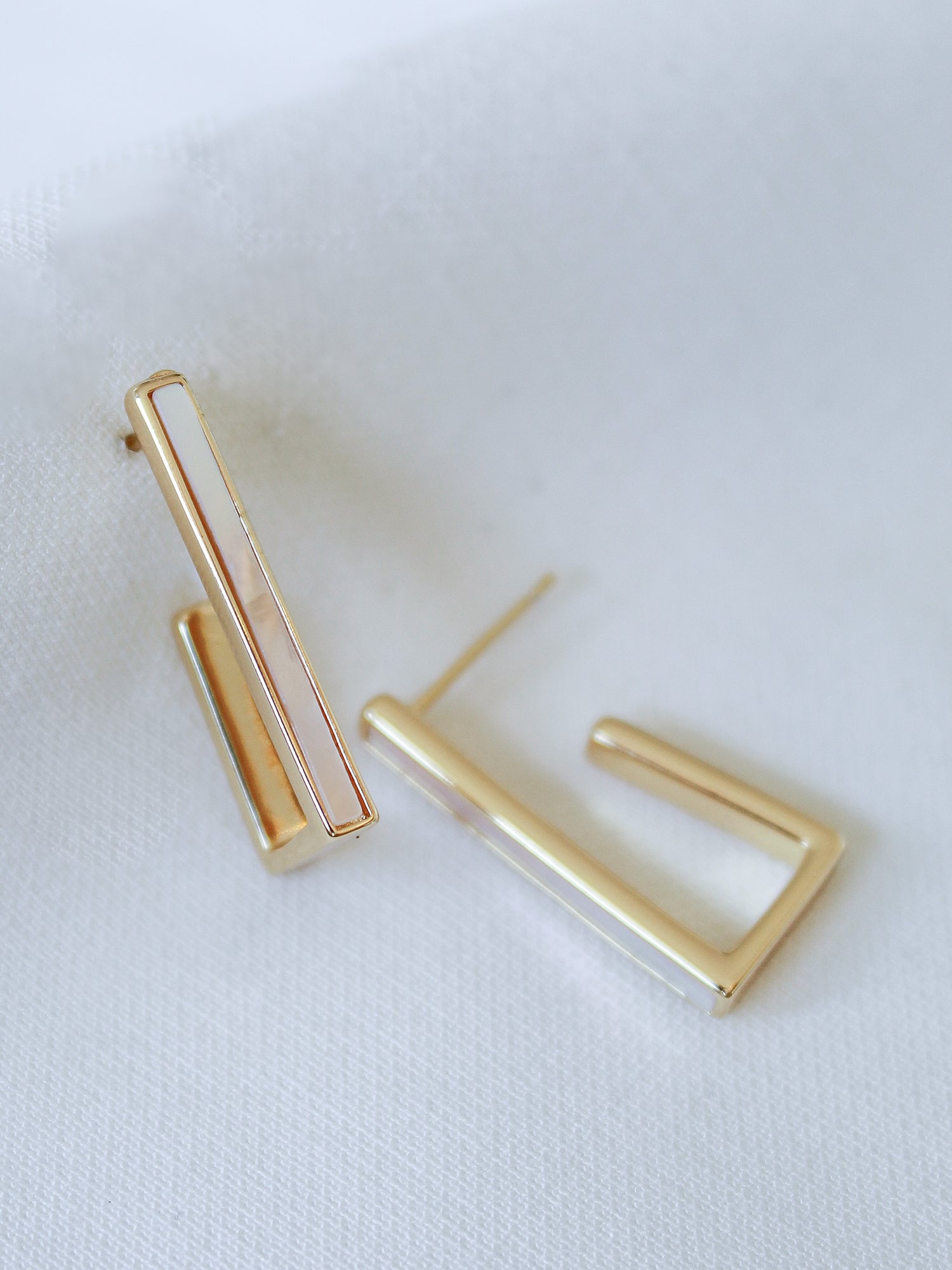 The Kai Earring by Kinsey Designs Archives features gold filled, minimalist rectangular and L-shaped designs, each 1 inch long, displayed on a white fabric background.