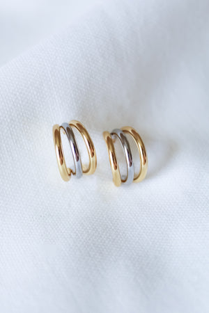 The Keera Mixed Earrings by Kinsey Designs—a pair of gold and silver .5" hoops—are displayed on soft white fabric, highlighting their timeless elegance.