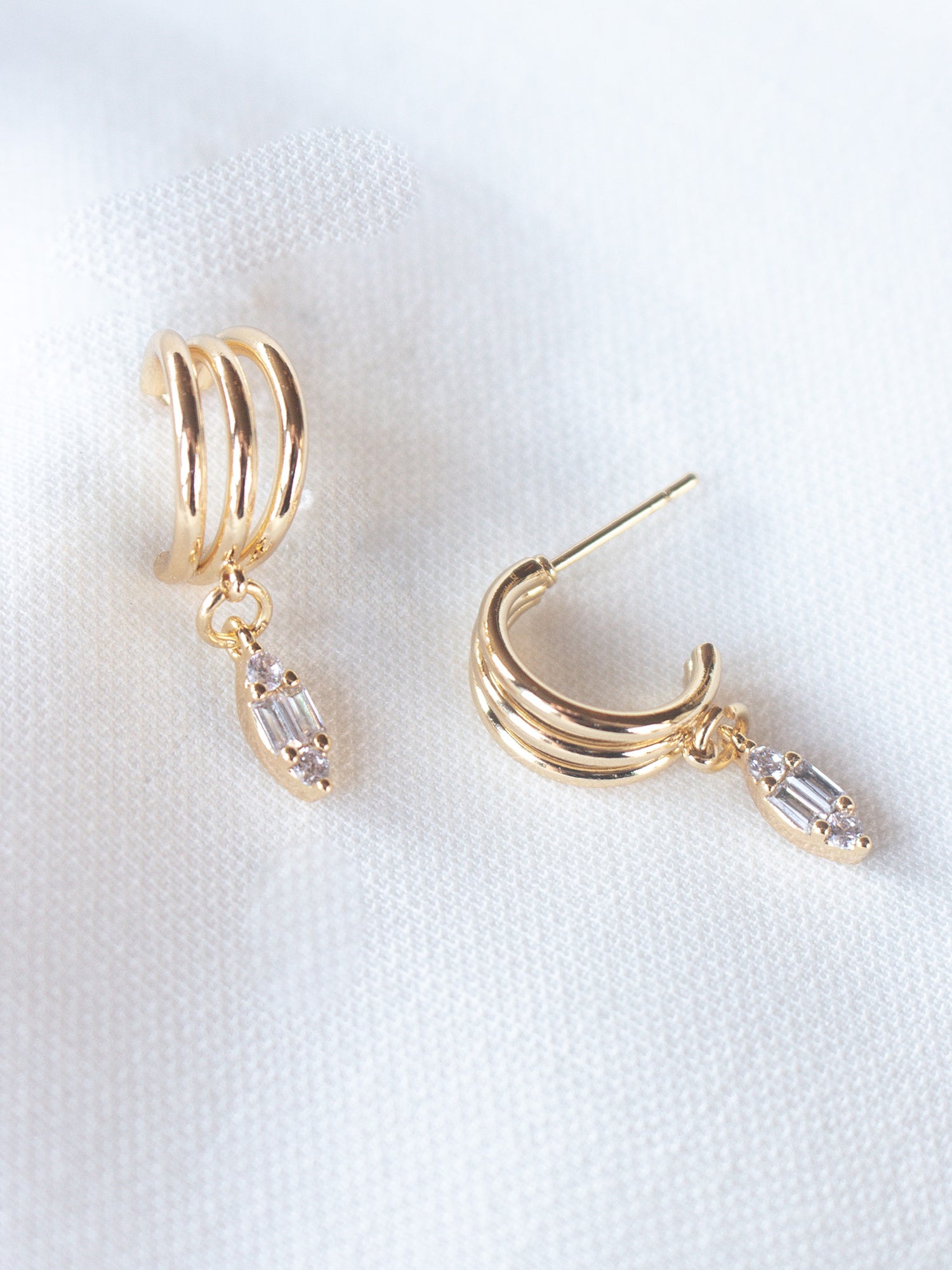 Add sparkle to your look with the Keira Drop Hoop by Kinsey Designs Archives—gold-filled hoops featuring three ridges and a clear cubic zirconia drop, shown on white fabric. Shop now at our exclusive sample sale!.