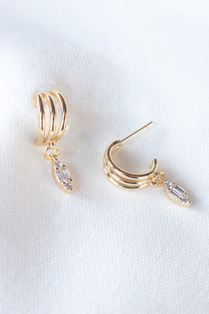 Add sparkle to your look with the Keira Drop Hoop by Kinsey Designs Archives—gold-filled hoops featuring three ridges and a clear cubic zirconia drop, shown on white fabric. Shop now at our exclusive sample sale!.