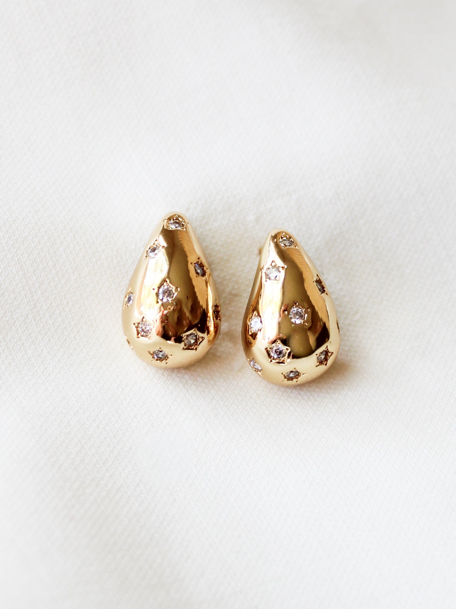 The Kline Dome Earring by Kinsey Designs Archives features gold-filled teardrops with small clear stones, shown on a soft white fabric. Earring length: 0.75 inches.