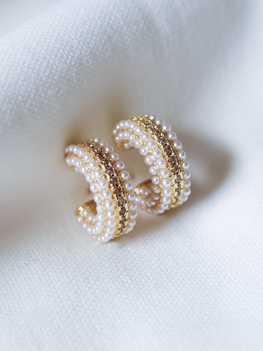 The Korey Pearl Hoops by Kinsey Designs are displayed on a soft white fabric, highlighting these classic pearl earrings in an elegant setting.