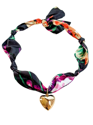 The Laquila Scarf Necklace by Kinsey Designs features a floral pattern, gold heart pendant, and adjustable design, elegantly tied in a bow.