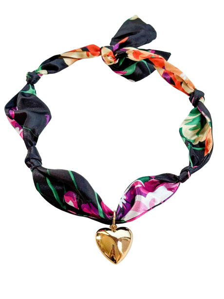 The Laquila Scarf Necklace by Kinsey Designs features a floral pattern, gold heart pendant, and adjustable design, elegantly tied in a bow.