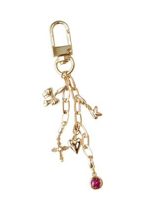 The Kinsey Designs Kinsey Bag Charm Chain features gold-filled charms—a butterfly, cross, heart, bird, and a pink gemstone—on a white background. This elegant accessory is perfect as a purse or bag charm.