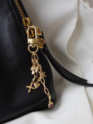 Close-up of a black leather bag with the Kinsey Designs Kinsey Bag Charm Chain, featuring a gold-filled chain and charm keychain attached to the zipper for a chic accessory detail.