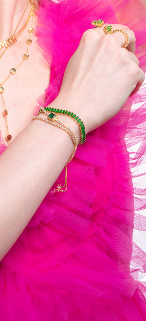 A hand wearing the Lara Bracelet - Emerald by Kinsey Designs Archives rests on a ruffled hot pink fabric dress.