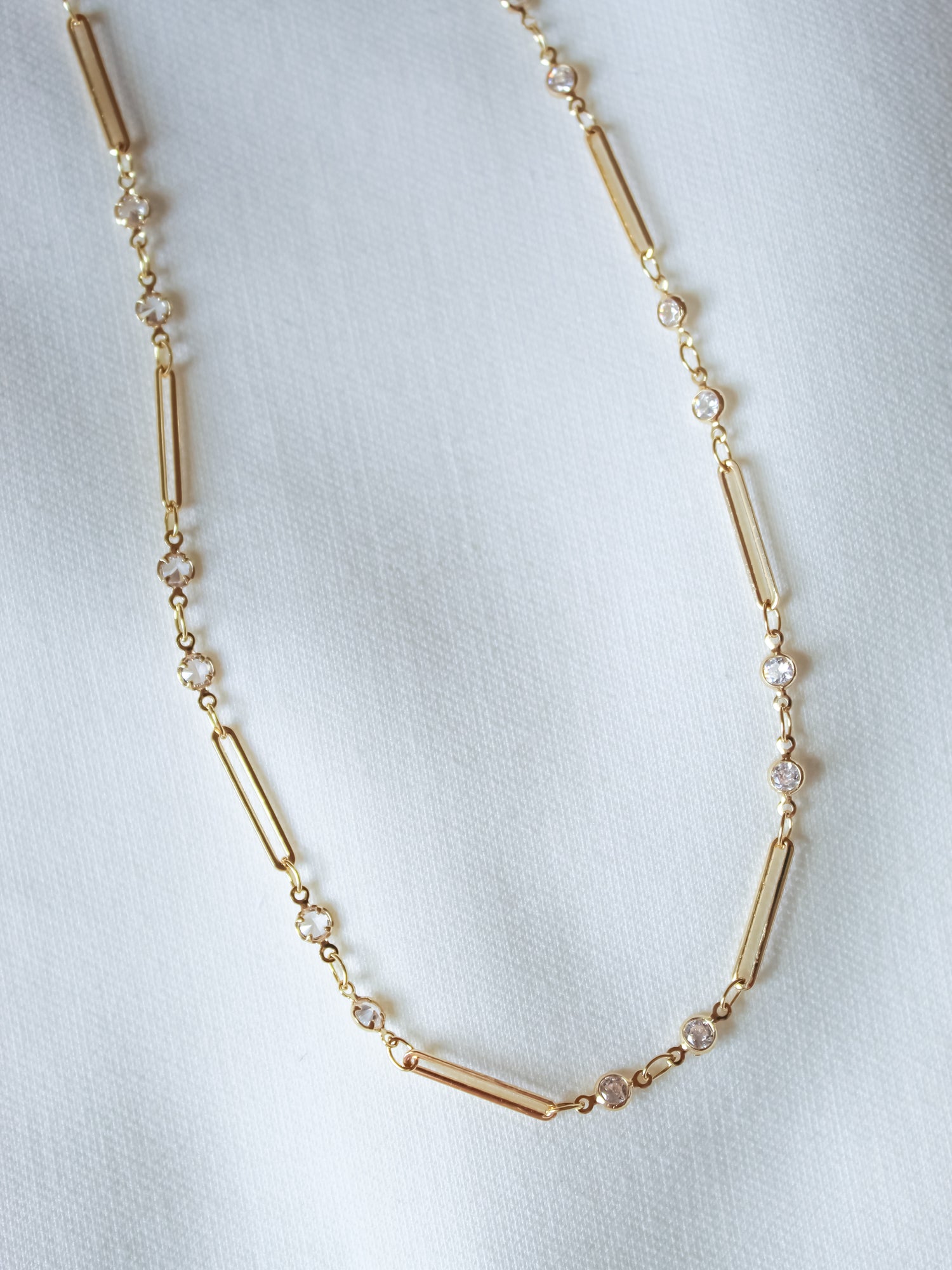 The Leander Necklace by Kinsey Designs features cylindrical and round gold filled beads, displayed on a white fabric background—an ideal pick for your next sample sale find.