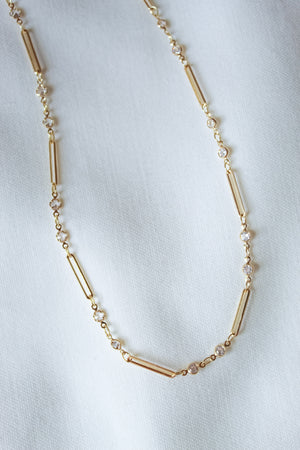 The Leander Necklace by Kinsey Designs features cylindrical and round gold filled beads, displayed on a white fabric background—an ideal pick for your next sample sale find.