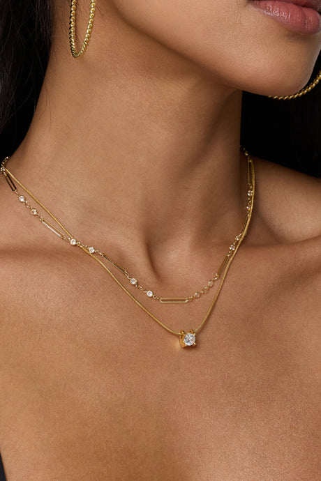 A woman wearing gold filled hoop earrings and the Kinsey Designs Leander Necklace, a layered gold chain with a round gemstone pendant—your perfect sample sale find.