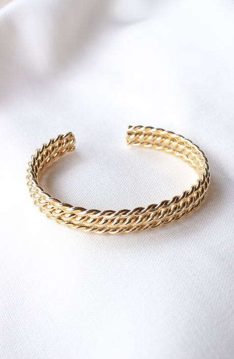 The Lenny Cuff by Kinsey Designs Archives, a gold filled braided adjustable bracelet, is displayed on a white fabric background.