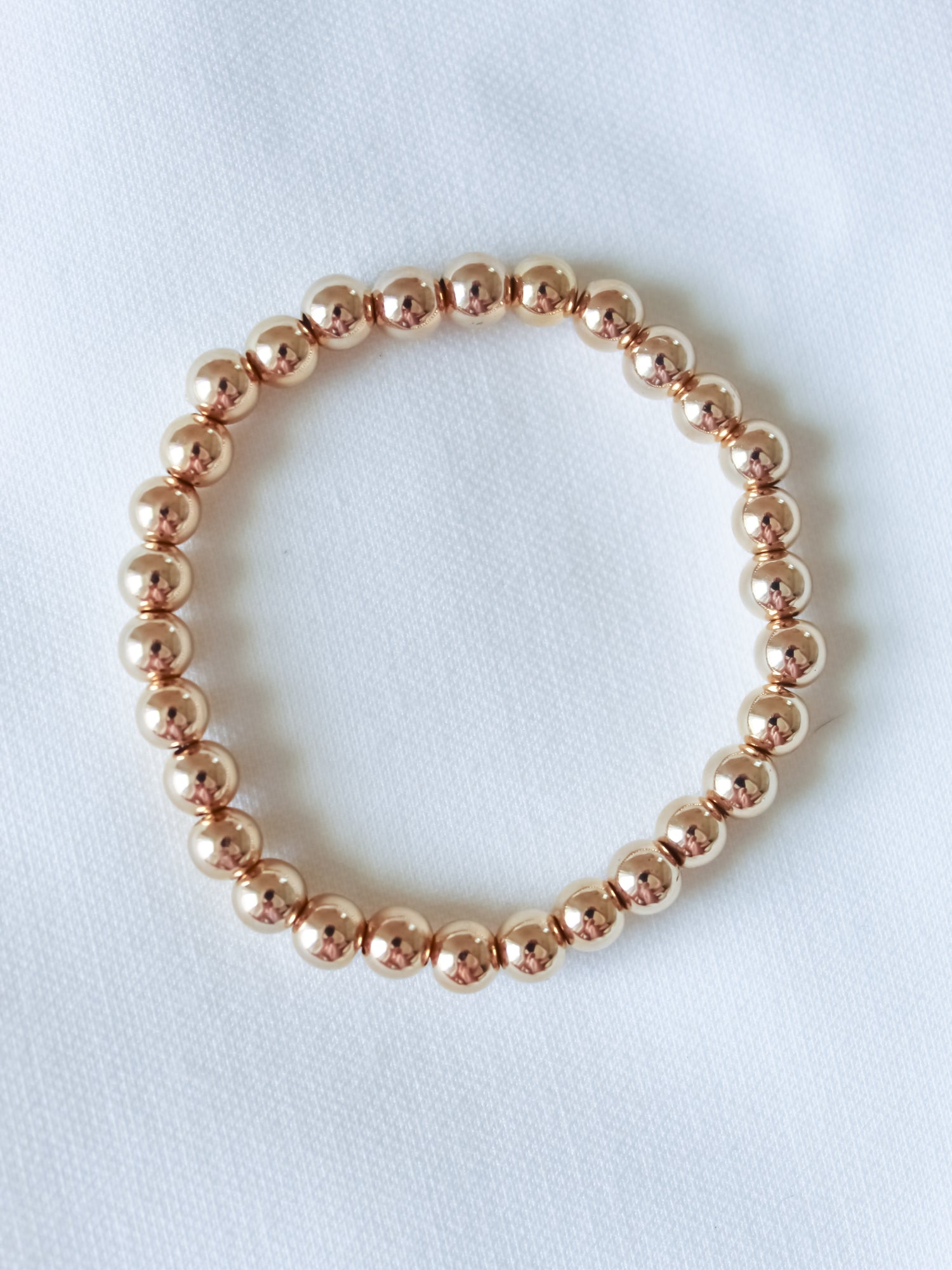 The Liam Stacking Bracelet by Kinsey Designs, shown in multiple sizes with gold-filled beads and adjustable stretch, is displayed in a circle on a white fabric background.