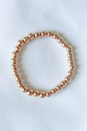 The Liam Stacking Bracelet by Kinsey Designs, shown in multiple sizes with gold-filled beads and adjustable stretch, is displayed in a circle on a white fabric background.