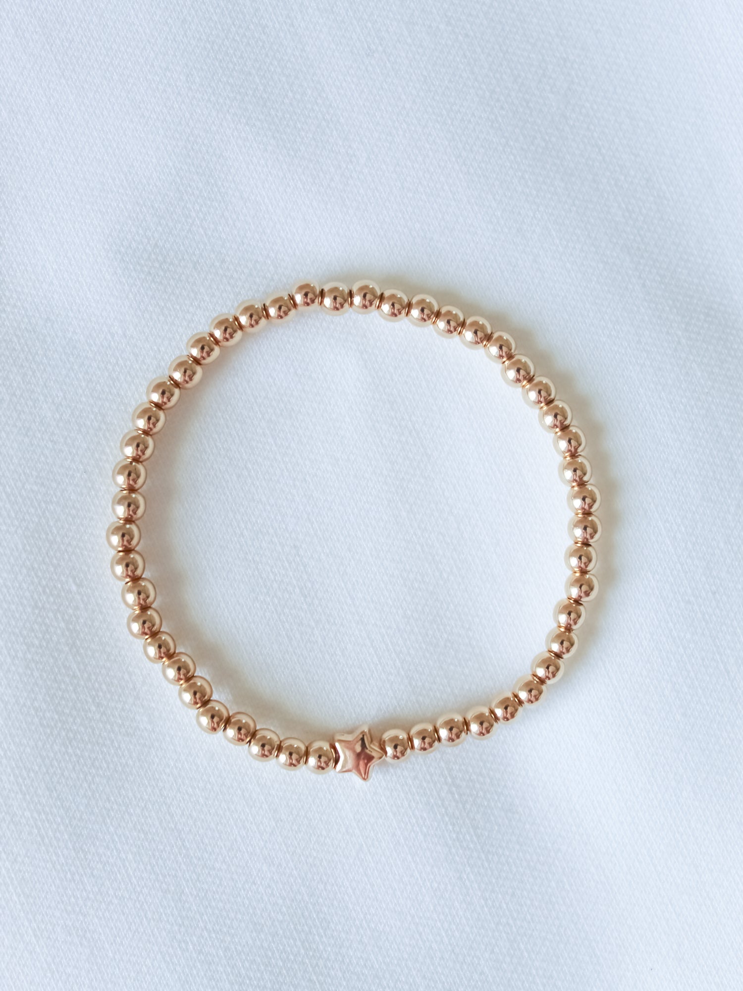 The Liam Stacking Bracelet by Kinsey Designs features gold-filled beads and a single star charm. Displayed on a white textured surface, this bracelet comes in multiple sizes with an adjustable stretch design for a comfortable fit.