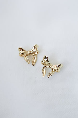 The Lova Studs by Kinsey Designs, featuring two shiny gold bows, make perfect feminine jewelry and are elegantly displayed against a plain white background.