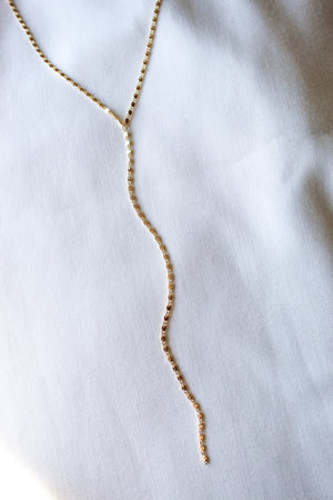 The Kinsey Designs Lula Lariat Necklace, a gold filled Y necklace, is displayed elegantly on a white fabric surface.