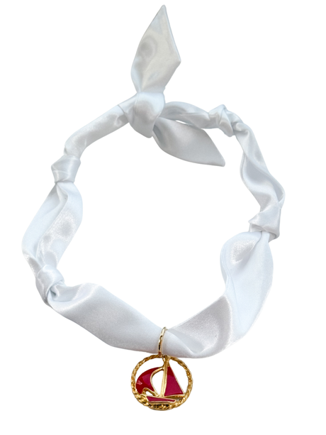 The Modena Scarf Necklace by Kinsey Designs features a white satin scarf with a knot and a gold and red sailboat vintage pendant, offering versatile style as an adjustable, one-of-a-kind scarf necklace.