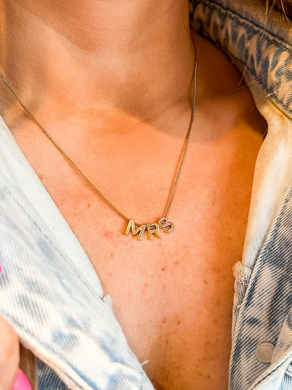 Close-up of a woman wearing the Kinsey Designs MRS Block Necklace with a light denim jacket and pink nail polish—perfect as a bride-to-be gift.