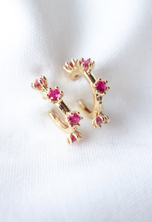 The Mae Huggie by Kinsey Designs Archives features gold filled hoops with small pink cubic zirconia stones, shown on a soft white fabric background.