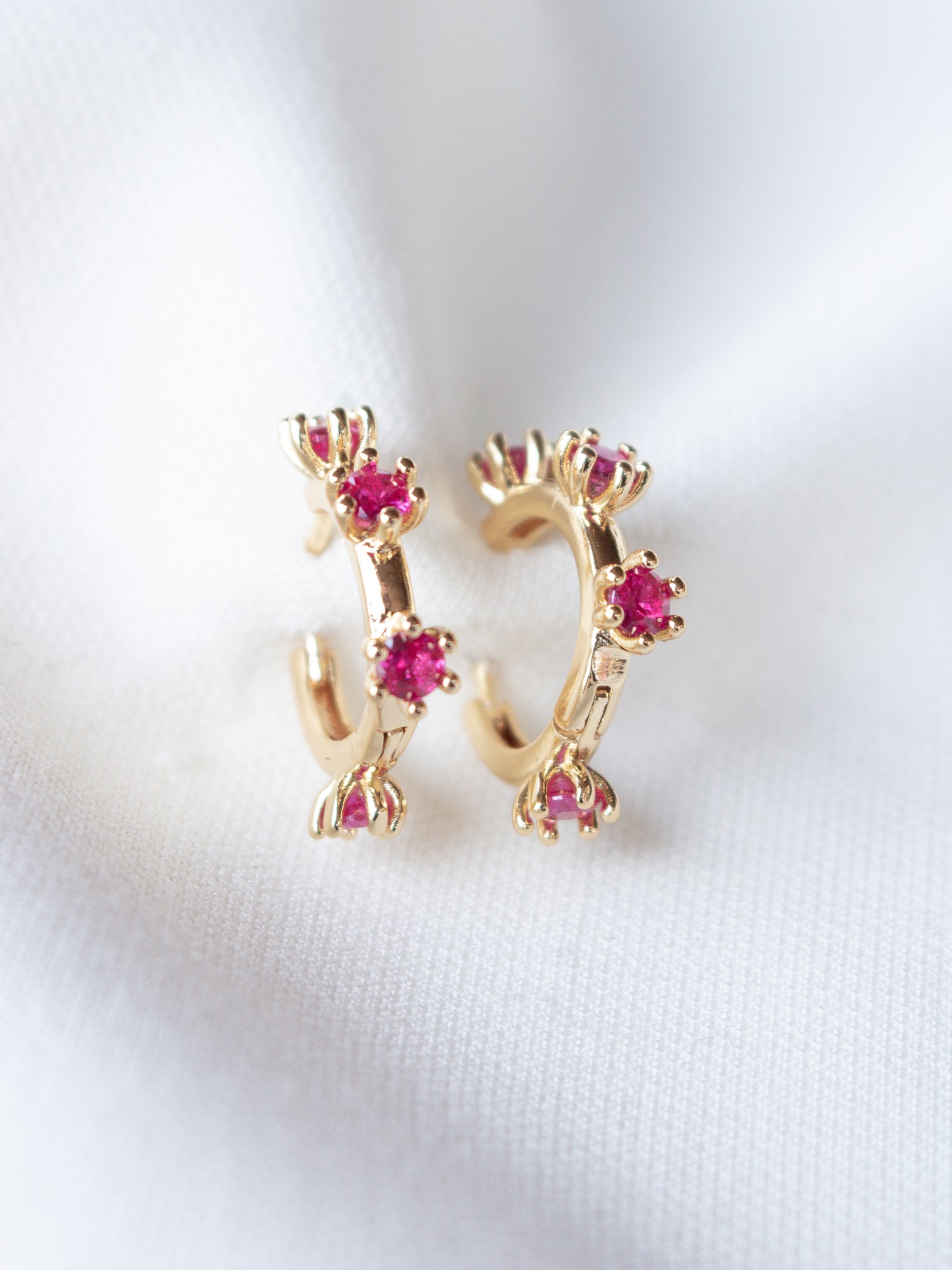 Mae Huggie gold filled hoop earrings from Kinsey Designs Archives, featuring small pink cubic zirconia gemstones on a white fabric background. Perfect for adding sparkle—shop this exclusive sample sale!.