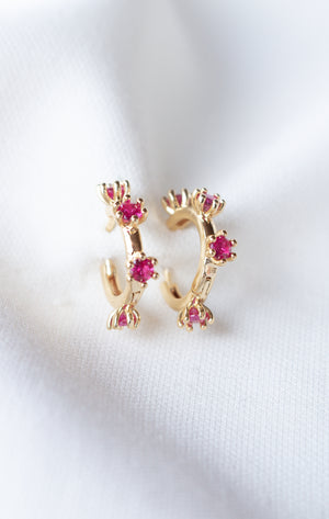Mae Huggie gold filled hoop earrings from Kinsey Designs Archives, featuring small pink cubic zirconia gemstones on a white fabric background. Perfect for adding sparkle—shop this exclusive sample sale!.