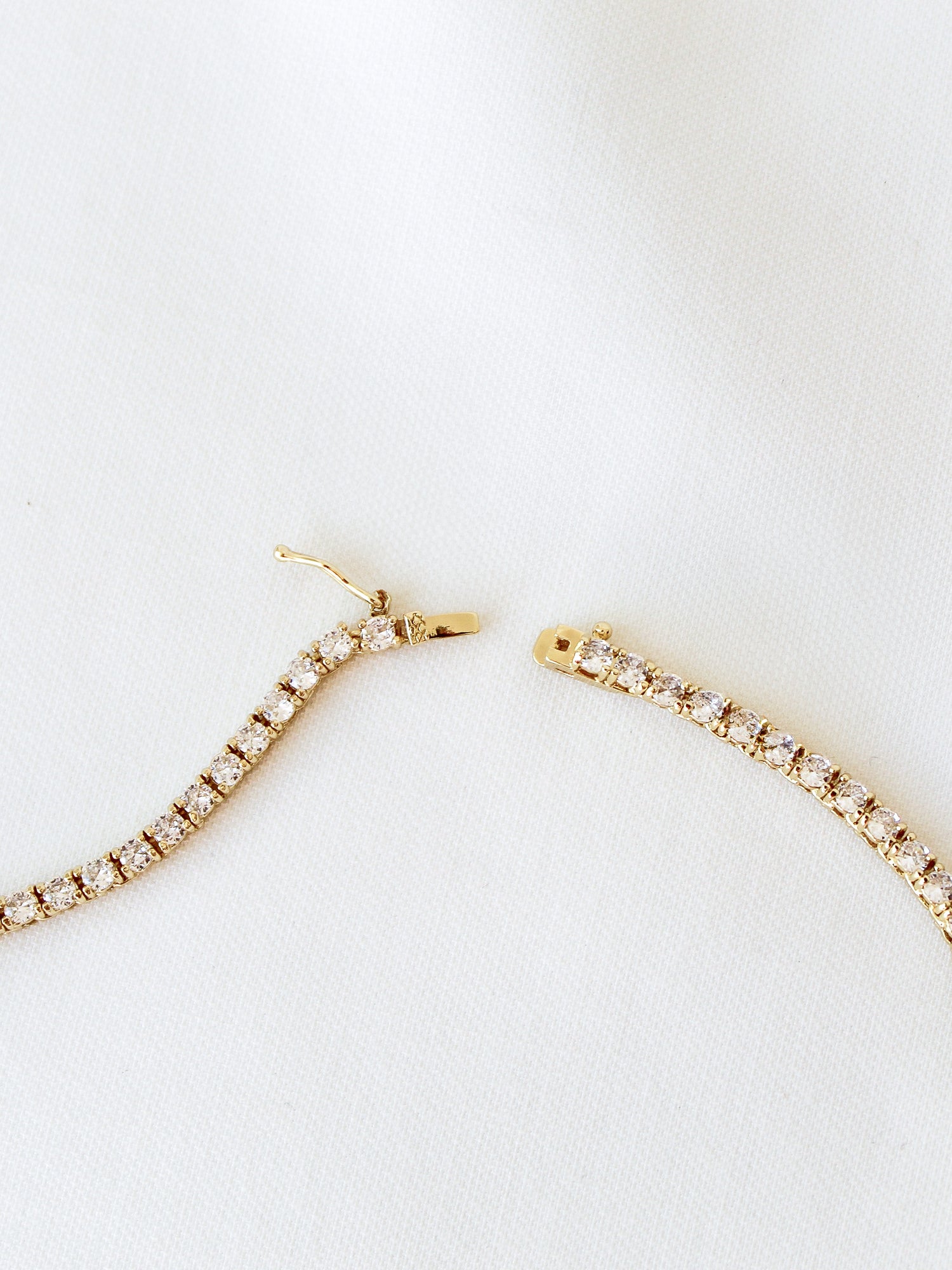 The Malia Tennis Necklace by Kinsey Designs Archives, shown unclasped on white fabric, pairs perfectly with a bracelet and is available now at our sample sale.