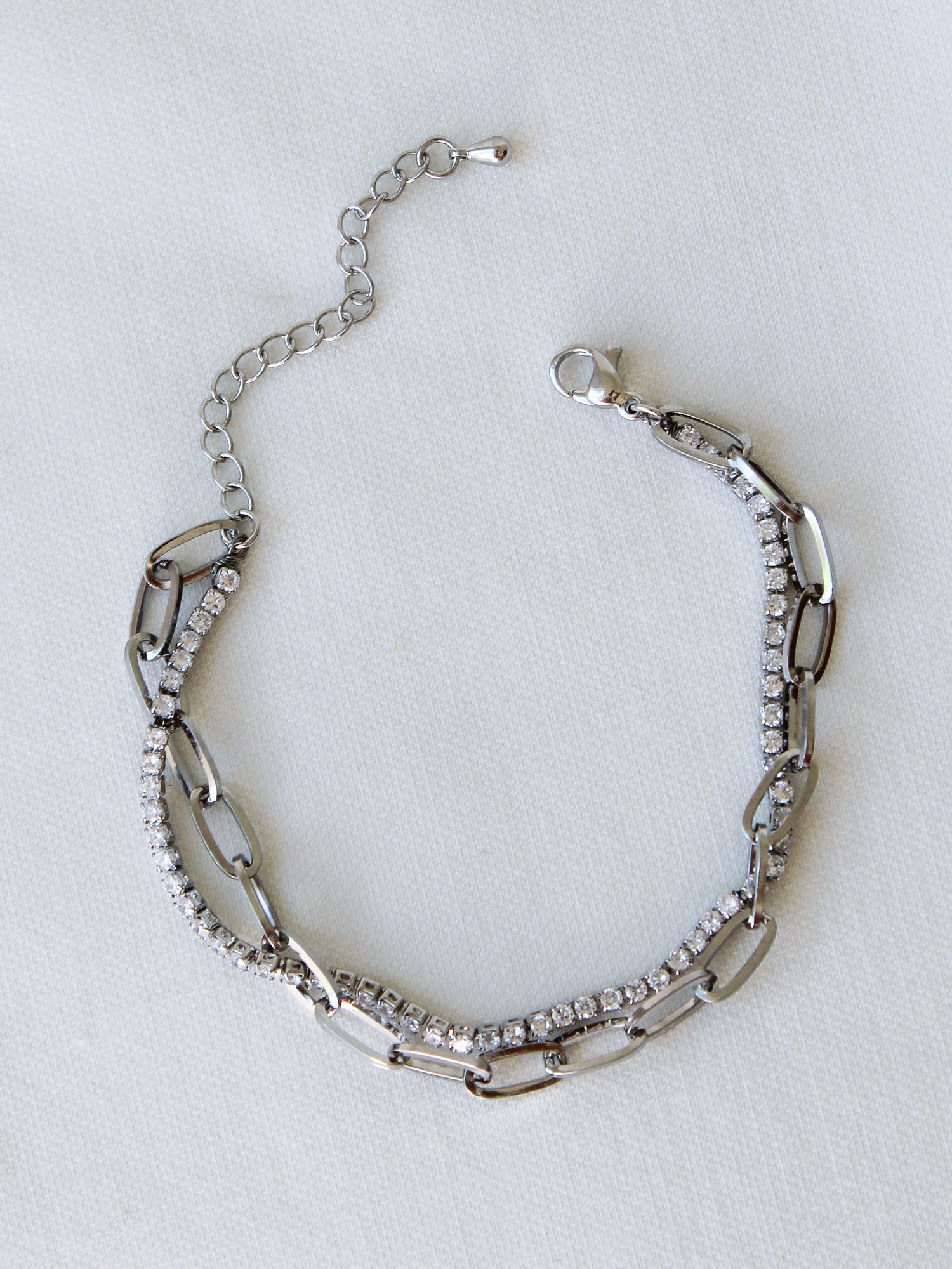 The Marc Tennis Bracelet by Kinsey Designs, featuring sparkling rhinestones and rhodium plating, is displayed on a white fabric background.