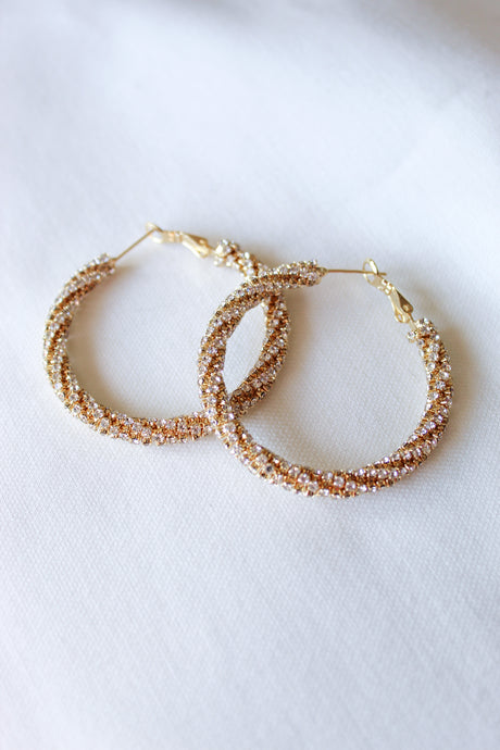 Two Marlowe Hoops by Kinsey Designs Archives—sparkly, gold-filled earrings with a textured, twisted design—are displayed on a white fabric background.