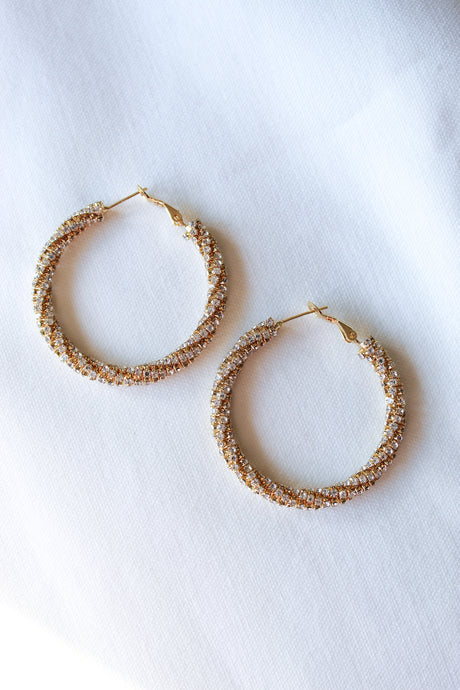 The Marlowe Hoop by Kinsey Designs Archives features gold-filled twisted hoops with a sparkling, textured finish, reminiscent of cubic zirconia earrings, elegantly displayed on white fabric.