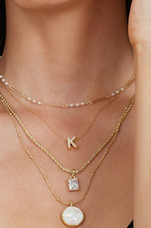 The Martin Necklace by Kinsey Designs Archives features four layered gold-filled chains with pearls, a K pendant, a rectangular cubic zirconia charm, and a circular charm on a 19" chain.