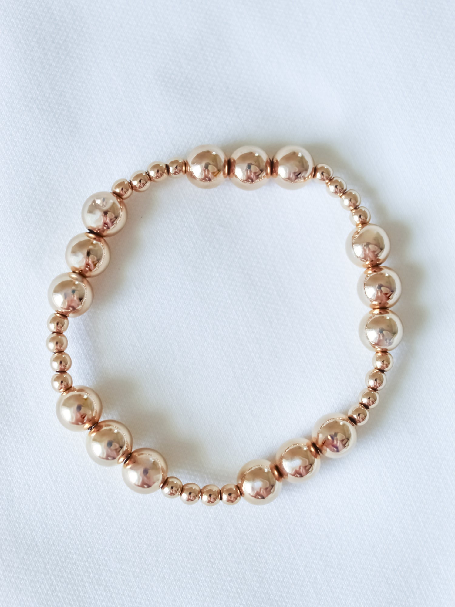 The Mia Bracelet by Kinsey Designs, a gold filled adjustable stretch piece, is displayed in a circle on white fabric—perfect for discovering at a sample sale.