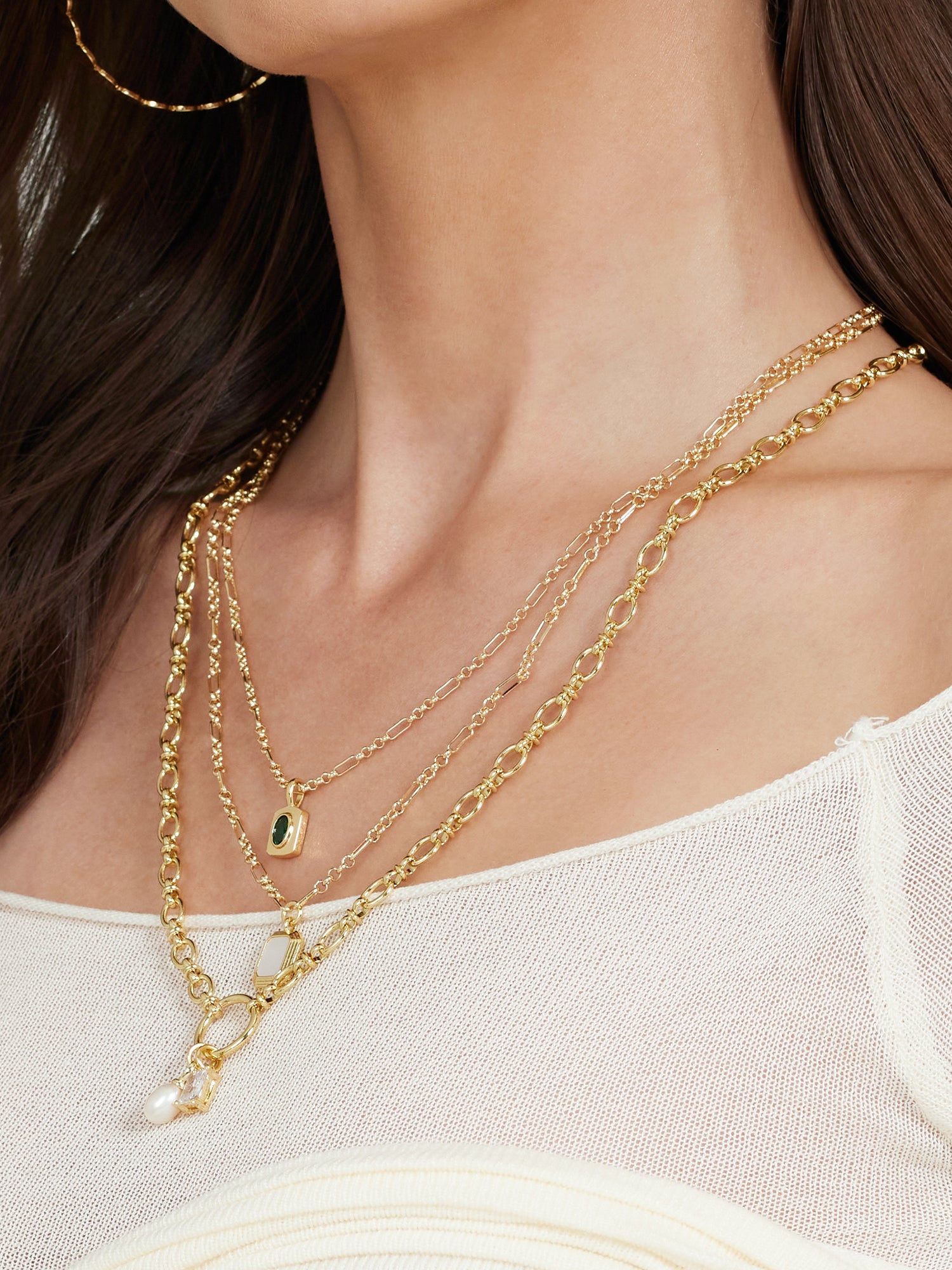 A woman in a cream off-shoulder top wears Kinsey Designs Archives' Mirabelle Pendant Necklace layered with a 20" gold-filled chain and pairs them with a gold hoop earring.
