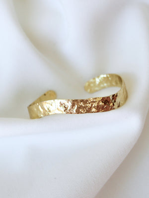The Molten Cuff Bracelet by Kinsey Designs Archives rests on white fabric, highlighting its elegant hammered gold filled shine. This adjustable, timeless piece is perfect for any occasion—grab it now in our exclusive sample sale!.