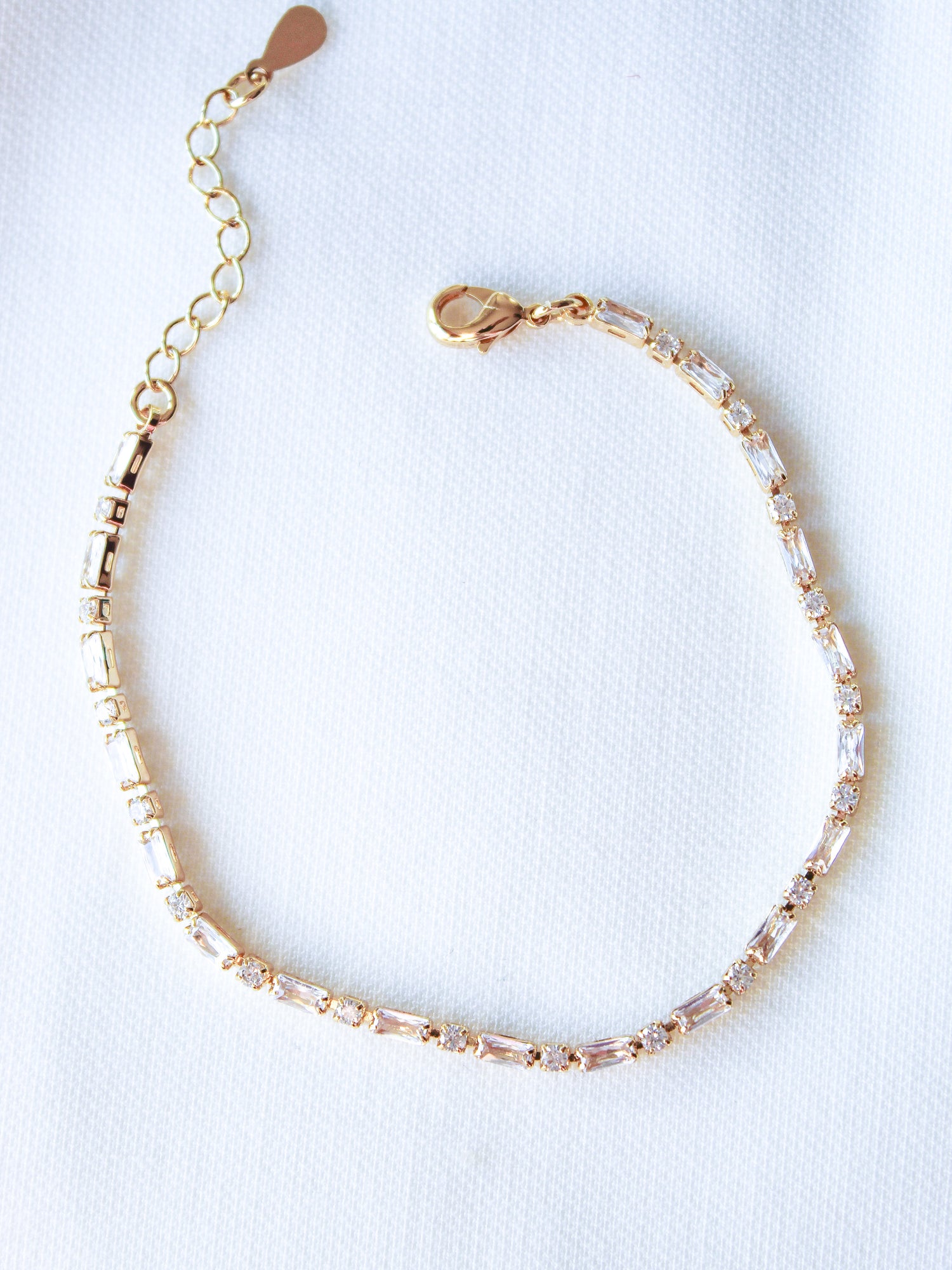 The Nora Bracelet by Kinsey Designs is a gold plated piece accented with sparkling cubic zirconia, showcased on a white fabric background.