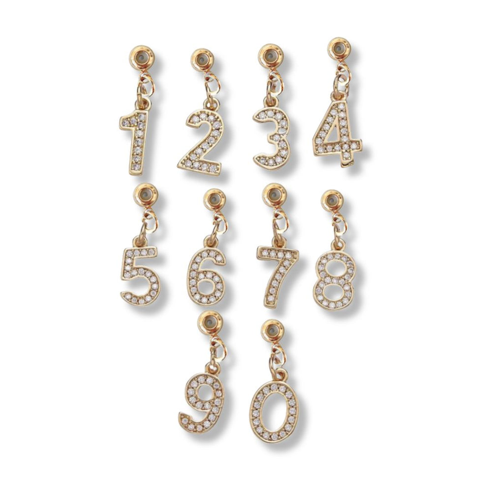 The Kinsey Designs Collection Numerical Grip Charm Number 0, featuring sparkling crystals, is displayed on a white background as part of a set with the numbers 0–9 arranged in two rows.