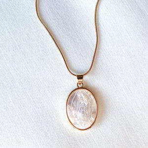 The Pippa Necklace by Kinsey Designs features a round pendant with a carved Madonna motif, displayed on a white fabric background.