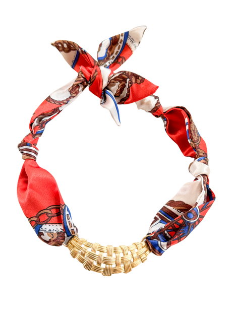 The Pordenone Scarf Necklace by Kinsey Designs features a gold woven pendant on a red patterned adjustable scarf, knotted at the top.