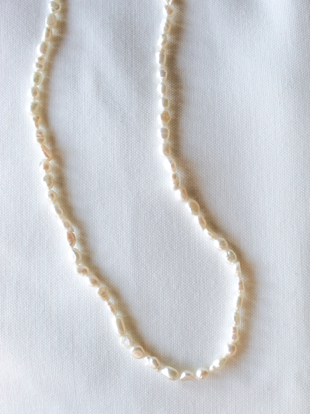 The Kinsey Designs Pearl Layering Necklace is displayed on textured white fabric, highlighting the elegance and craftsmanship of this artisanal pearl jewelry.