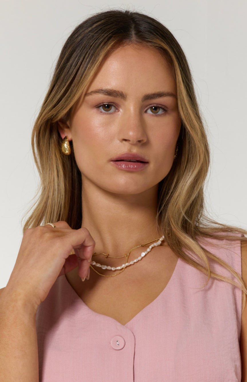 Woman with wavy blonde hair wearing a pink sleeveless top and the Kinsey Designs Pearl Layering Necklace, an artisanal gold and natural pearl jewelry set.