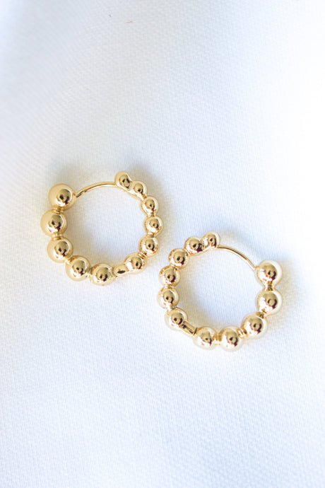 The Pebble Huggie by Kinsey Designs Archives are gold-plated beaded hoop earrings with a 0.75" circumference, shown on a white fabric background.