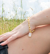 The Coral Pearl Bracelet by Kinsey Designs Archives, featuring a mother-of-pearl charm, shines on a person’s wrist outdoors in a grassy field.