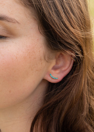 Close-up of a woman's ear wearing Kinsey Designs' Tide Climber—gold filled jewelry with a curved turquoise design—paired with a small gold hoop, making these pieces perfect for a sample sale discovery.