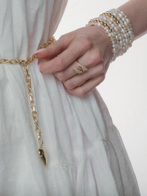 Woman in a white dress wearing the Kinsey Designs Poppy Puffy Heart Necklace, a gold oval link chain belt, pearl bracelets, and a ring on her hand.