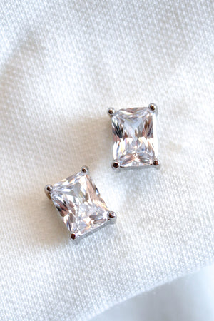 Kinsey Designs' Prism Studs shine on a white textured fabric. These gold filled earrings with sparkling Cubic Zirconia add a touch of elegance to any look.